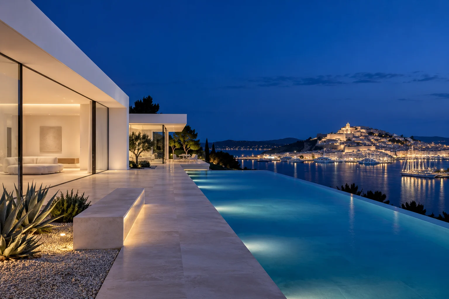 Infinity pool edge at blue hour aligned with the lit old town of Dalt Vila across the harbour